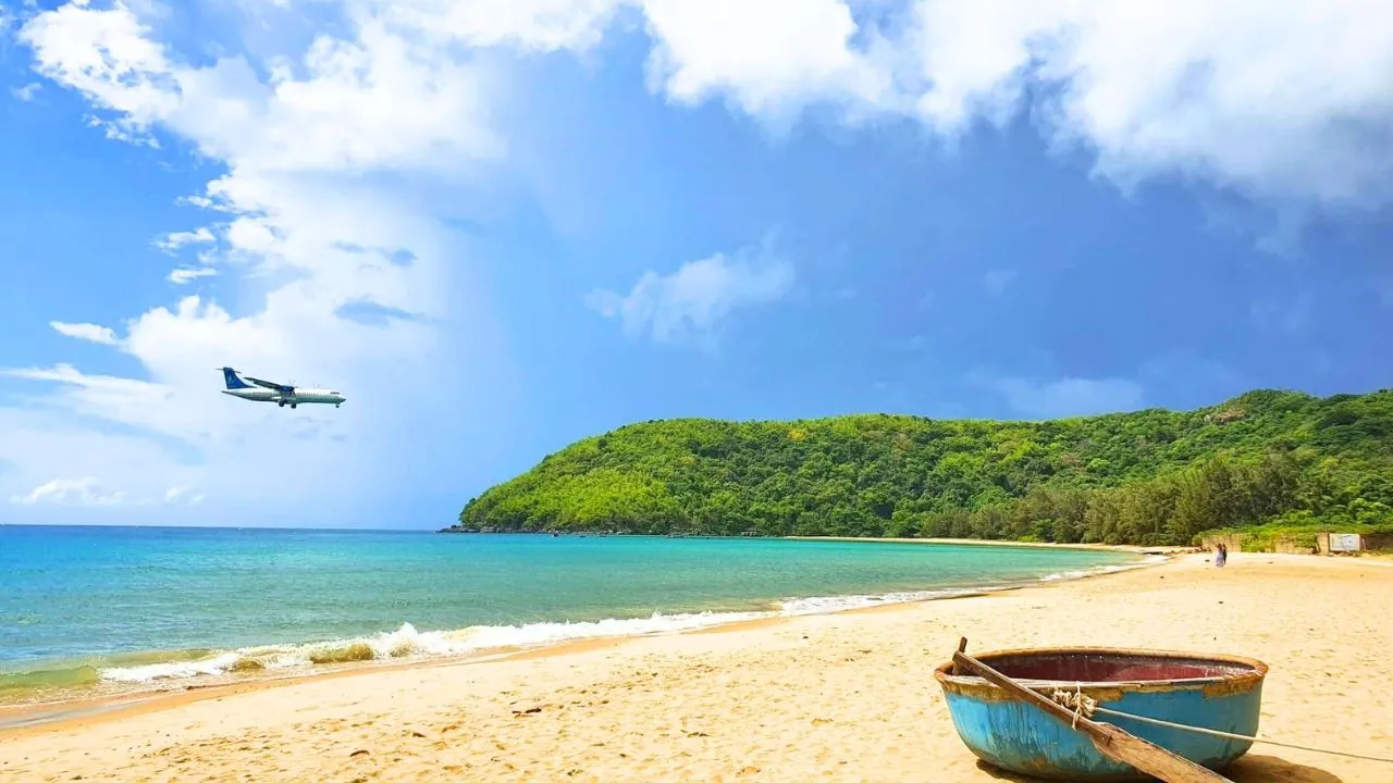 Bãi Đầm Trầu nước xanh, máy bay đang bay thấp phía trên hàng cây chuẩn bị hạ cánh.